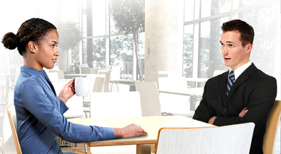 A casually dressed woman and a man in a suit sitting at a table in a working environment